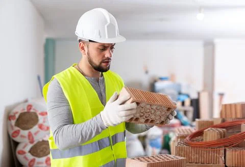 Young builder inspects and stacks bricks on top of each other Stockfoto's