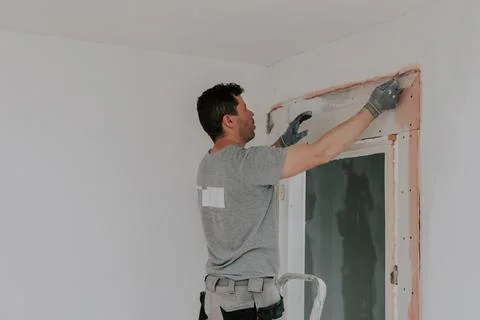 A young builder installs a construction mesh for puttying on a wall. Stock Photos