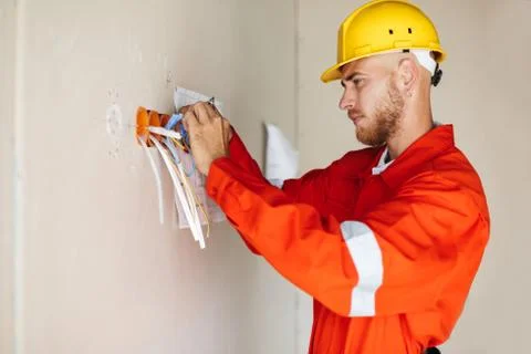 Young builder in orange work clothes and yellow hardhat thoughtf Stock Photos
