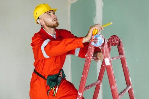 Young builder in orange work clothes and yellow hardhat standing Stock Photos