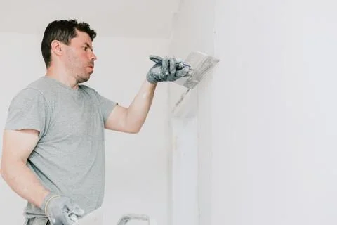 A young builder is plastering the wall above the doorway. Stock Photos