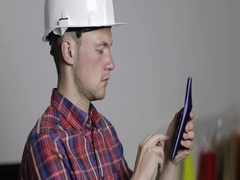 A young builder in a white helmet counts on a calculator. Stock Footage 77148669