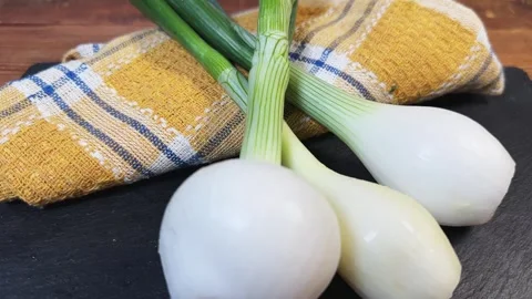 Young bulb onions with green stems on flat slate plate 動画素材 339791994