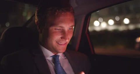 Young business man texting on on cell phone in backseat of car at night in city Stock Footage