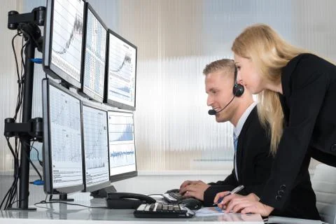 Young business people analyzing data displayed on computer screens in office Stock Photos