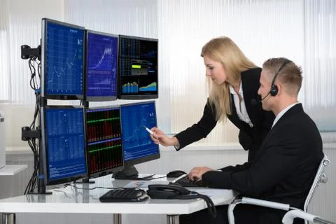 Young business people analyzing data displayed on computer screens in office Stock Photos