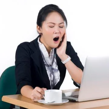 Young business woman yawning at her desk with a cup of coffee Stock Photos