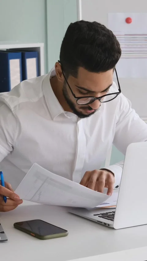 Young businessman analyzing documents and working on a laptop in the office Stock Footage 328129026