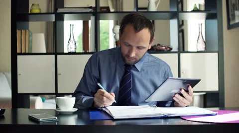 Young businessman chatting on tablet computer and reading documents at home HD Stock Footage 45430016