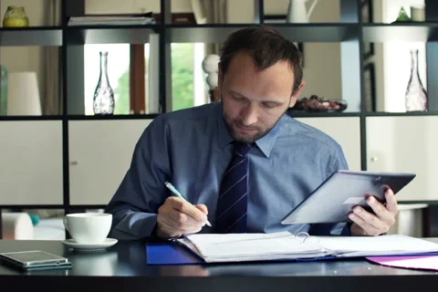 Young businessman chatting on tablet computer and reading documents at home Stock Footage 45430019
