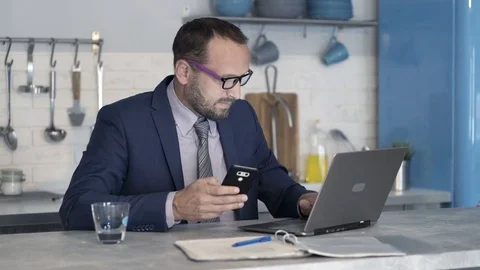 Young businessman checking data on smartphone and laptop at home Stock Footage 82139492