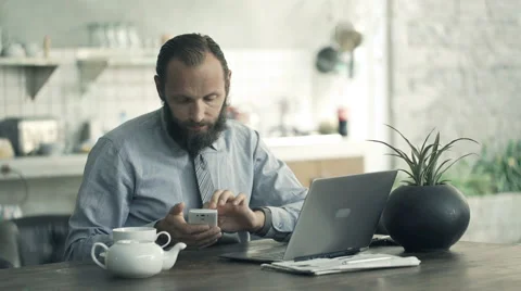 Young businessman comparing data on laptop and smartphone by table in kitchen Stock Footage 64056488