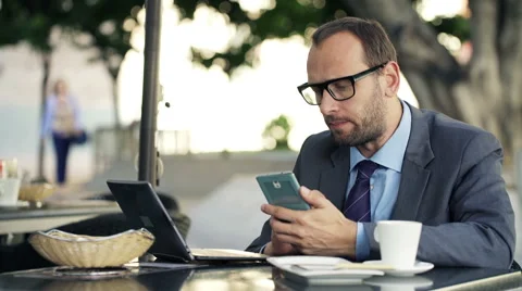 Young businessman comparing data on smartphone and laptop in cafe city HD Video stock 47438437