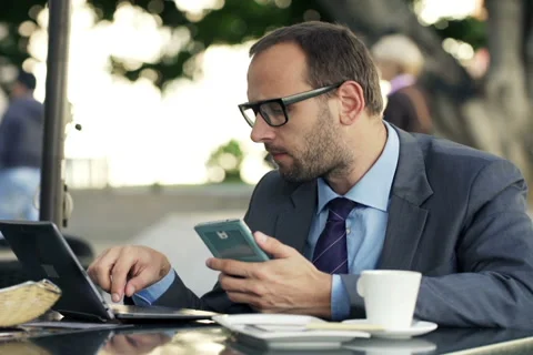 Young businessman comparing data on smartphone and laptop in cafe city NTSC Stock Footage 47438464