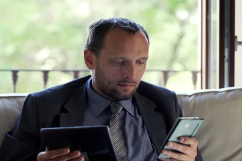 Young businessman comparing data on tablet computer and smartphone at home NTSC Stock Footage 46216435