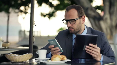 Young businessman comparing data on tablet computer and smartphone in cafe HD Stock Footage 47091734