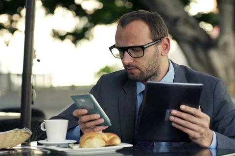 Young businessman comparing data on tablet computer and smartphone in cafe NTSC Stock Footage 47091790