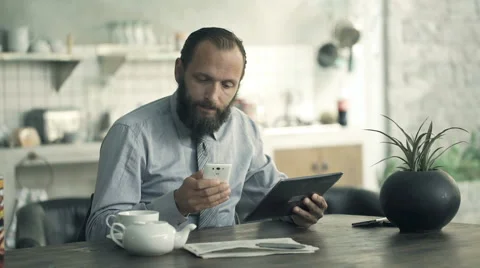 Young businessman comparing data on tablet and smartphone by table in kitchen Stock Footage 64056648