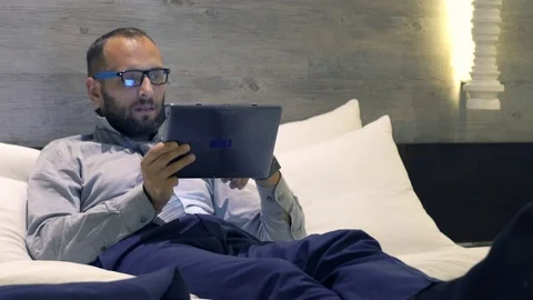 Young businessman comparing data on tablet and smartphone lying on bed Stock Footage 71275717