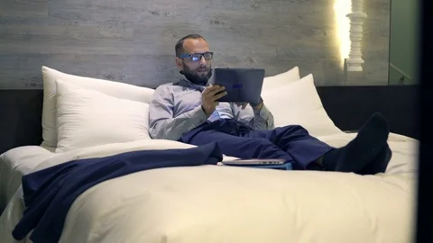Young businessman comparing data on tablet and smartphone lying on bed, 4K Stock Footage 71279243