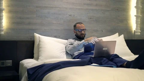 Young businessman comparing data on tablet and laptop lying on bed, 4K Stock Footage 71279360