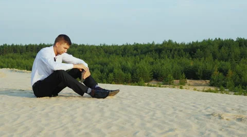 Young businessman drinking alcohol from flasks sitting on the sand. Concept - Stock Footage 65987725