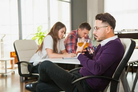 Young businessman drinks tea while his collegues on backgroung work hard 库存照片