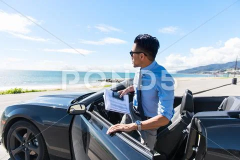 Young Businessman Getting Out Of Car At Coastal Parking Lot With Paperwork