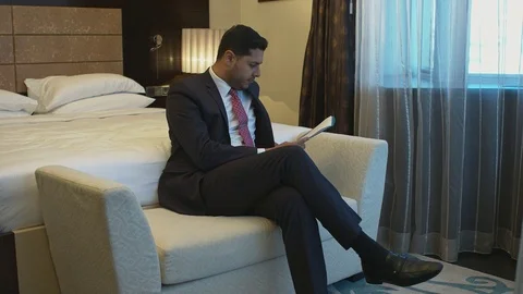 Young businessman going through papers sitting at his hotel room Stock Footage 80360752