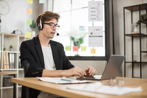 Young businessman in headset using laptop computer during video call working in Stock Photos