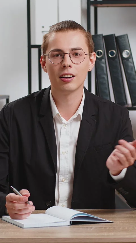 Young businessman looking to camera and writing down on diary in video chat at Stock Footage 320992836