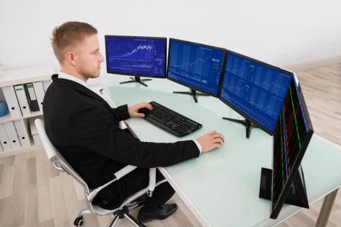 Young Businessman Looking At Graph On Multiple Computer Screen Foto stock