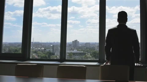 Young businessman looking through a large window at the city and cloudy sky. Stock Footage 63574638