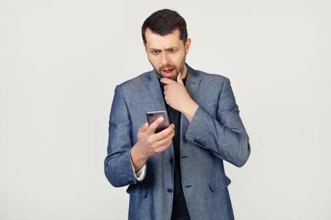 Young businessman man with a beard in a jacket using a smartphone scared shoc Stock-Fotos