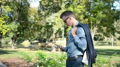 Young businessman outside in the park using mobile phone smartphone, putting 스톡 동영상 95040319
