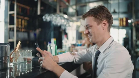 A young businessman sitting and using smartphone at the bar in the restaurant Stock Footage 217987856