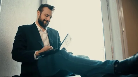 Young businessman sitting on the window and working on laptop Stock Footage 76016653