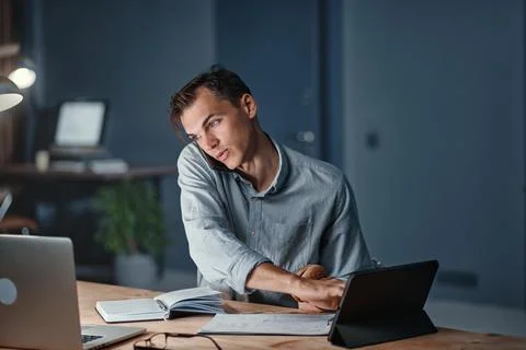 Young businessman snacking on a hamburger while working on a new project. Stock Photos