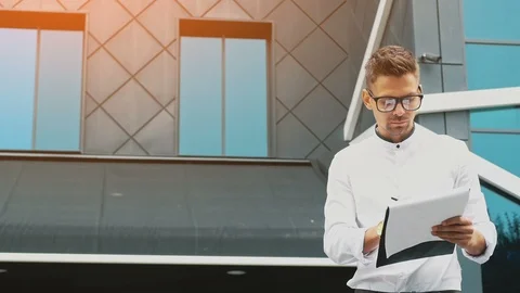 A young businessman stands at the office with a folder of documents in his hands Stock Footage 102498673