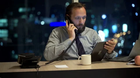Young businessman with tablet computer talking on phone in office at night Stock Footage 56934728