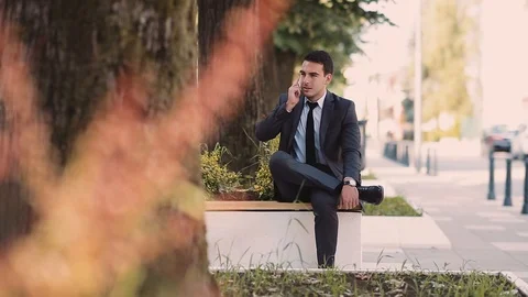 Young Businessman Talking At Phone While Sitting At Bench Stock Footage 87404777
