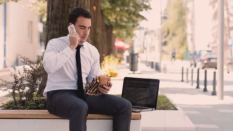 Young Businessman Talking On Phone While Eating And Using Laptop Stock Footage 87409741