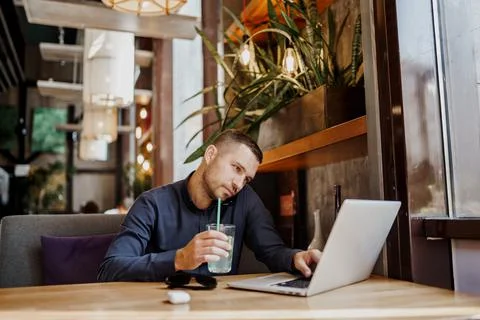 Young businessman is talking on phone while working on laptop in restaurant Stock Photos