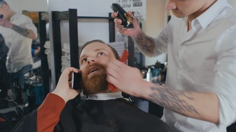 Young businessman talking on smartphone while getting haircut at hair salon Video stock 128809100