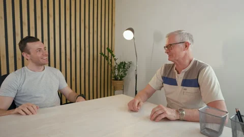 Young businessman talks to elderly client sitting at desk Stock Footage 201240267