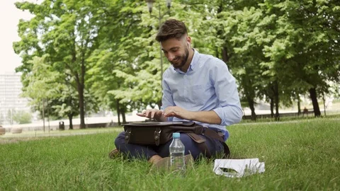 Young businessman typing on tablet while sitting in the park during lunch bre Stock Footage 112867933