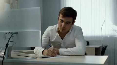 Young businessman using desktop computer and writing down information in notepad Video stock 111944534