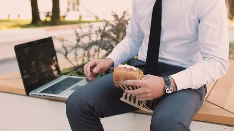 Young Businessman Using Laptop While Eating And Drinking Coffee To Go Stock Footage 87408727