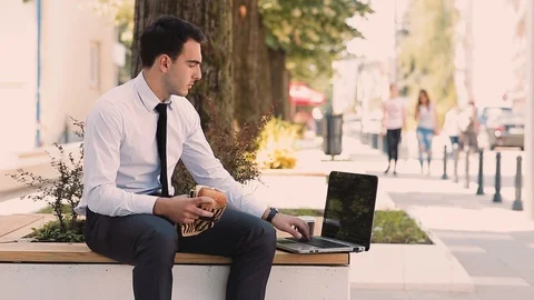 Young Businessman Using Laptop While Eating And Drinking Coffee To Go Stock Footage 87409093