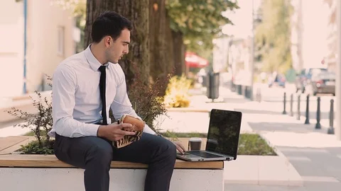 Young Businessman Using Laptop While Eating And Drinking Coffee To Go Stock Footage 87409365